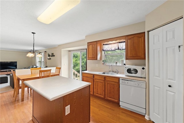 kitchen with pendant lighting, sink, white appliances, a kitchen island, and light wood-type flooring