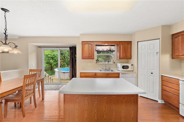 kitchen with pendant lighting, white appliances, a center island, and light wood-type flooring