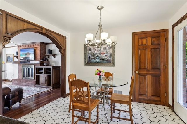 dining area featuring a notable chandelier, plenty of natural light, a brick fireplace, and hardwood / wood-style floors