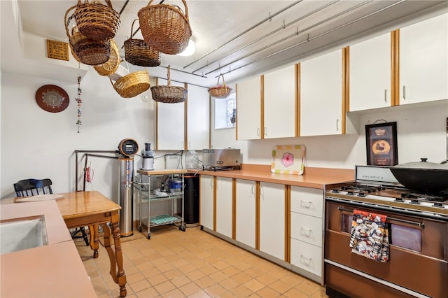 kitchen featuring light tile patterned flooring, white range with gas stovetop, and white cabinets