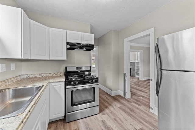 kitchen with white cabinets, sink, range hood, appliances with stainless steel finishes, and light hardwood / wood-style flooring