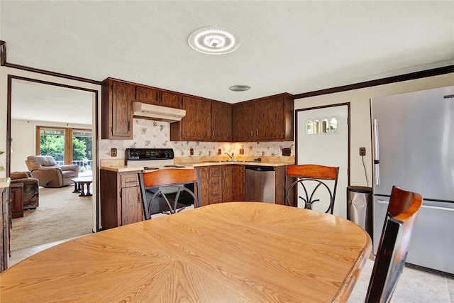 kitchen featuring crown molding, decorative backsplash, appliances with stainless steel finishes, light colored carpet, and dark brown cabinetry