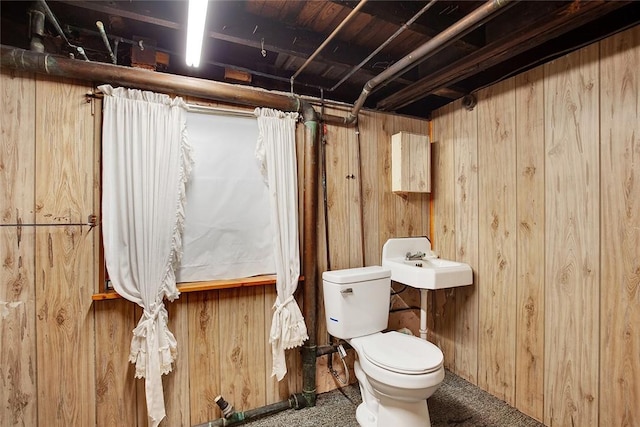 bathroom featuring toilet, wood walls, and sink