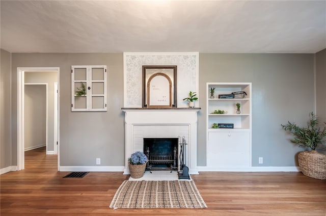 living room featuring built in shelves, a brick fireplace, and hardwood / wood-style floors