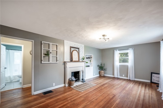 unfurnished living room with hardwood / wood-style floors, built in shelves, and a brick fireplace