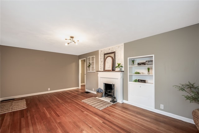 unfurnished living room with a fireplace, wood-type flooring, an inviting chandelier, and built in features