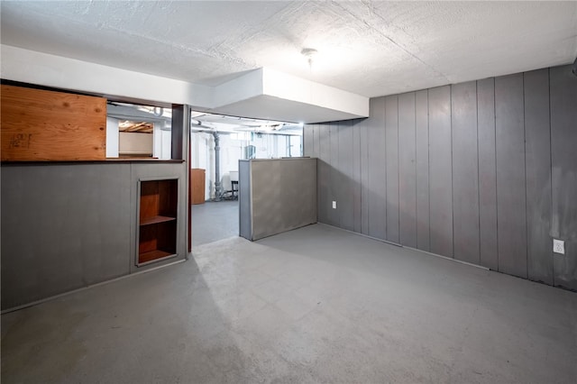 basement with a textured ceiling, built in features, and wooden walls