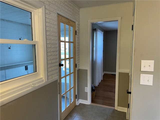 doorway to outside with french doors, dark tile patterned floors, crown molding, and brick wall