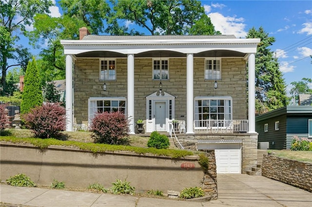 neoclassical home featuring an attached garage, central air condition unit, concrete driveway, stone siding, and a chimney