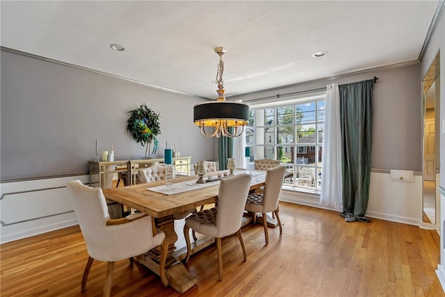 dining space featuring ornamental molding, light wood-type flooring, a wainscoted wall, and an inviting chandelier