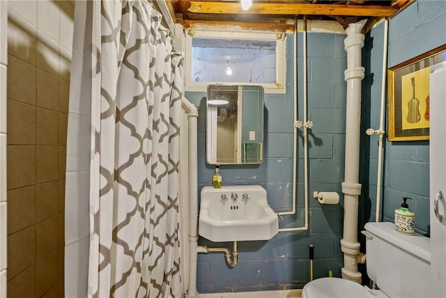 bathroom featuring curtained shower, a sink, toilet, and concrete block wall