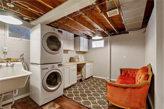 washroom with stacked washer / drying machine, cabinet space, visible vents, a sink, and baseboards