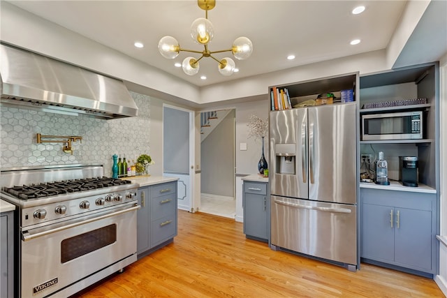 kitchen with appliances with stainless steel finishes, tasteful backsplash, light hardwood / wood-style floors, decorative light fixtures, and custom range hood