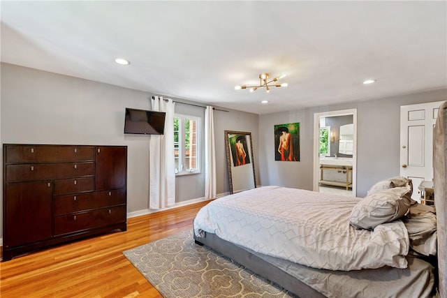 bedroom with ensuite bath, light hardwood / wood-style flooring, and a notable chandelier