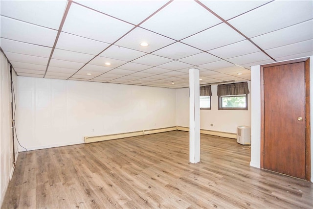 basement with a drop ceiling, a baseboard heating unit, and hardwood / wood-style flooring