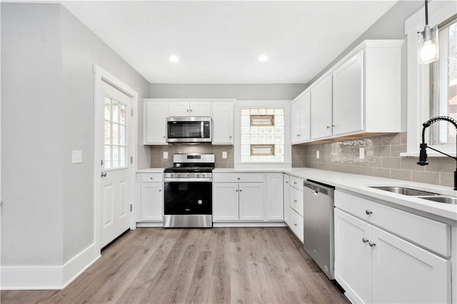 kitchen with a sink, stainless steel appliances, light wood-style floors, white cabinets, and decorative backsplash