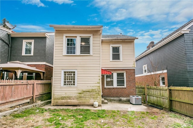 back of property with a patio area, a fenced backyard, brick siding, and central AC