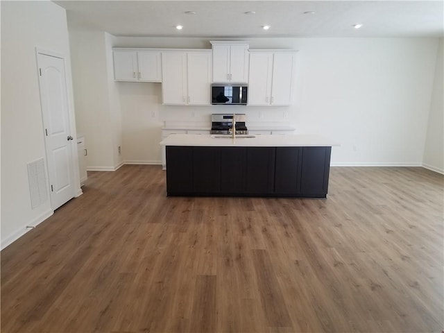 kitchen featuring a kitchen island with sink, white cabinets, stainless steel appliances, and light hardwood / wood-style floors