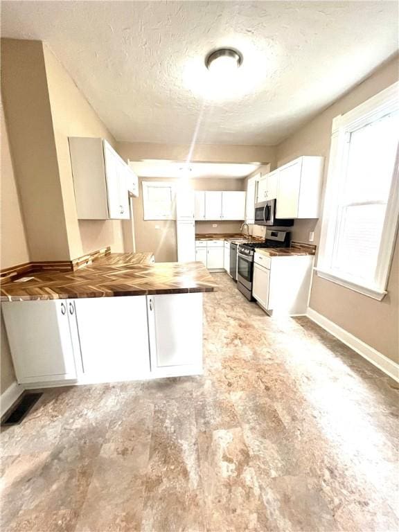 kitchen featuring butcher block counters, white cabinetry, a textured ceiling, and appliances with stainless steel finishes