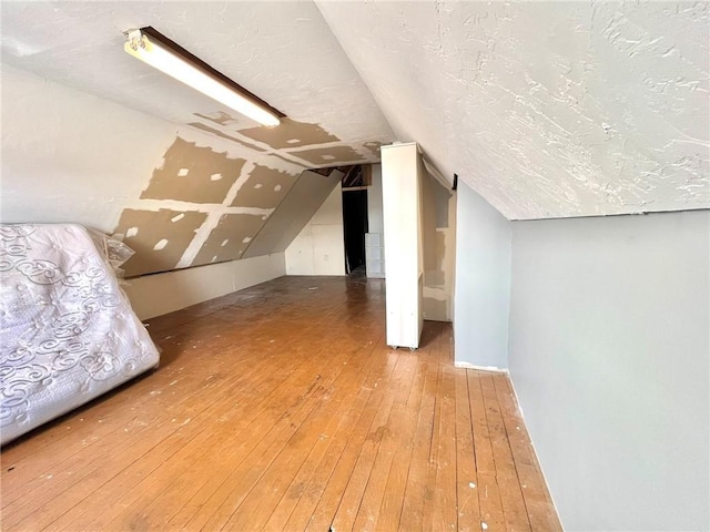 additional living space with hardwood / wood-style flooring, lofted ceiling, and a textured ceiling