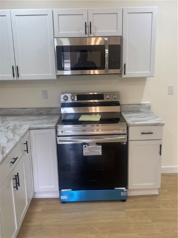 kitchen featuring light wood-type flooring, appliances with stainless steel finishes, light stone countertops, and white cabinetry