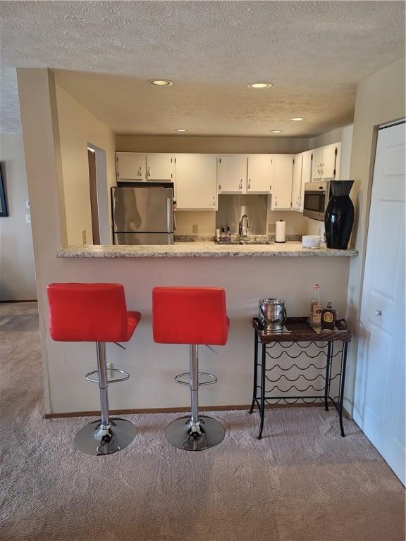 kitchen featuring carpet floors, white cabinets, a textured ceiling, and appliances with stainless steel finishes