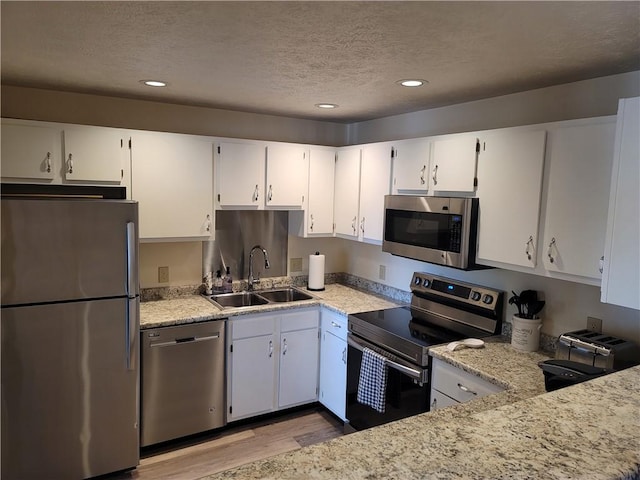 kitchen featuring light stone countertops, white cabinetry, stainless steel appliances, sink, and light wood-type flooring