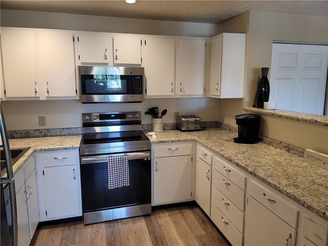 kitchen featuring white cabinets, light wood-type flooring, appliances with stainless steel finishes, and light stone counters