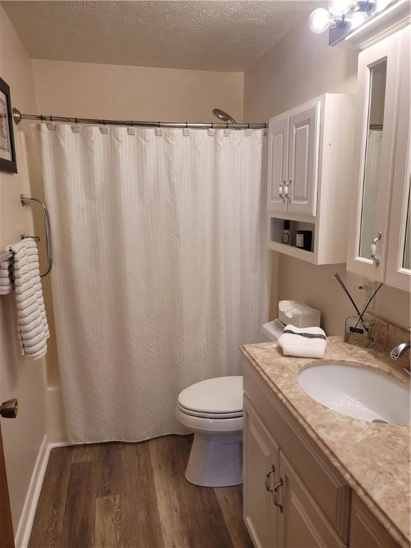 full bathroom with toilet, vanity, hardwood / wood-style flooring, a textured ceiling, and shower / tub combo with curtain