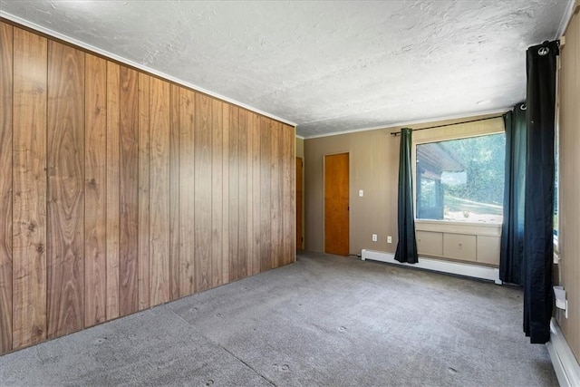 spare room with baseboard heating, light colored carpet, wood walls, and a textured ceiling