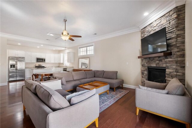 living room featuring a stone fireplace, dark wood-type flooring, ceiling fan, and ornamental molding