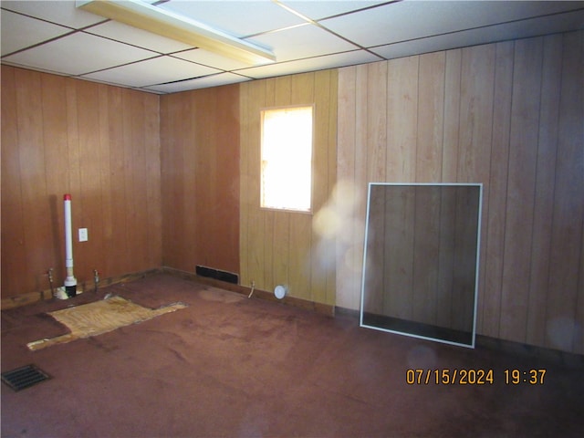 carpeted spare room with a paneled ceiling and wooden walls