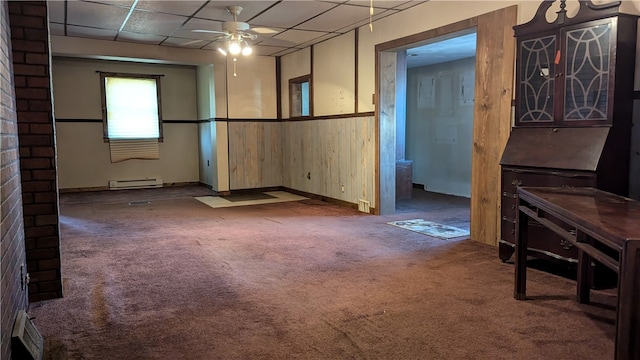 carpeted living room with ceiling fan, a baseboard radiator, a drop ceiling, and wood walls