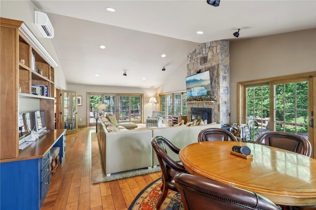 dining area with a wall mounted AC, a stone fireplace, wood-type flooring, and lofted ceiling