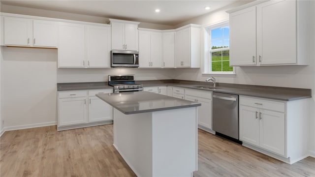 kitchen with appliances with stainless steel finishes, light hardwood / wood-style floors, white cabinetry, a kitchen island, and sink