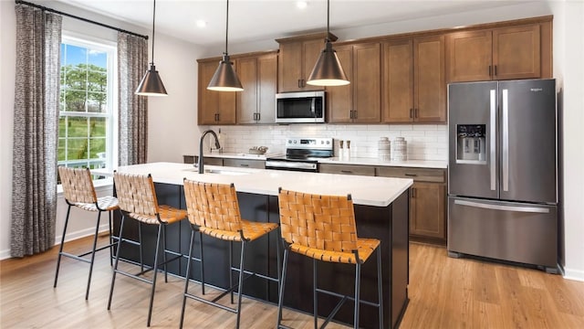 kitchen featuring light hardwood / wood-style floors, appliances with stainless steel finishes, decorative backsplash, and an island with sink