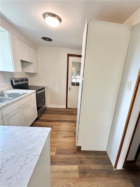 kitchen with wood-type flooring, sink, white cabinetry, and stainless steel range with electric stovetop