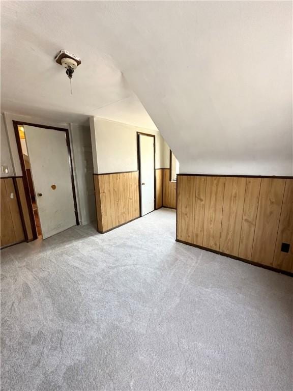 bonus room with vaulted ceiling, light colored carpet, and wood walls