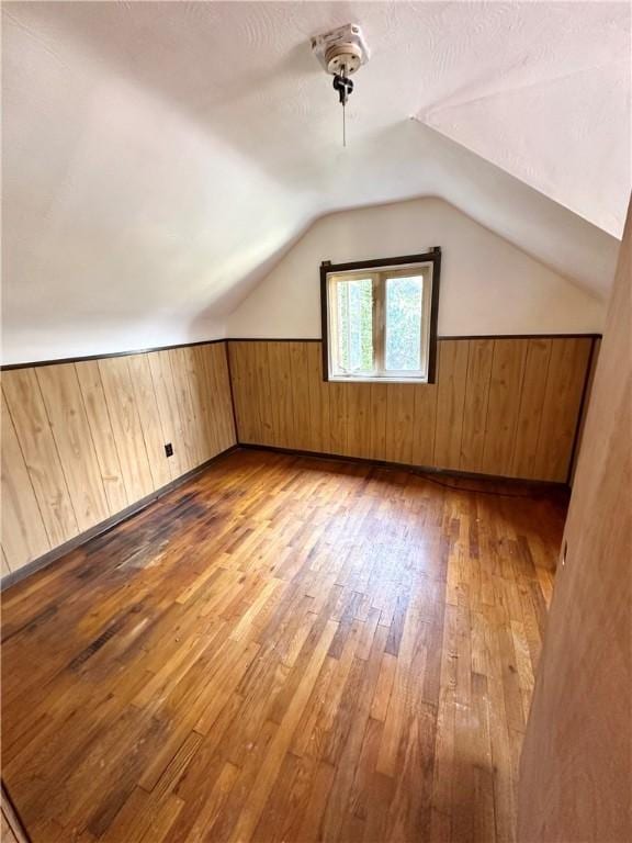 bonus room with lofted ceiling, light wood-type flooring, wooden walls, and a textured ceiling