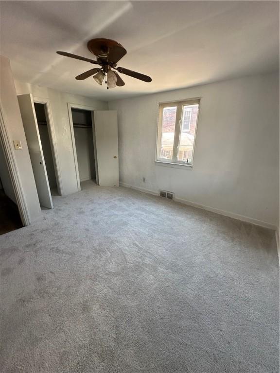 unfurnished bedroom featuring ceiling fan, carpet flooring, and multiple closets