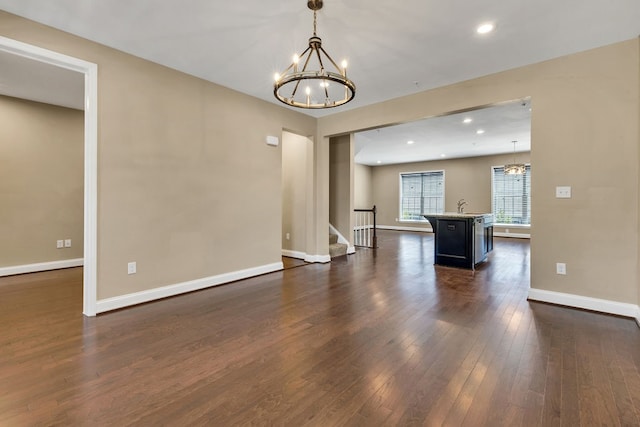 unfurnished living room featuring an inviting chandelier, sink, and dark hardwood / wood-style flooring