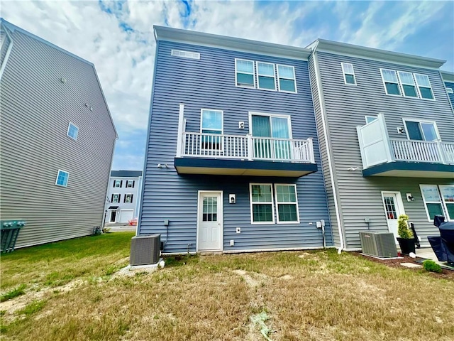 rear view of house with cooling unit, a balcony, and a yard