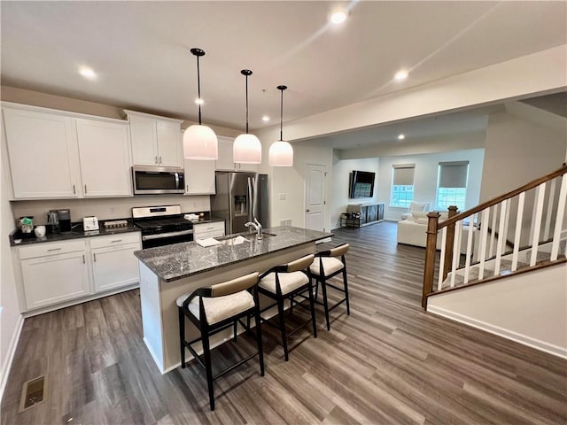 kitchen with a kitchen island with sink, a kitchen breakfast bar, sink, dark stone countertops, and stainless steel appliances