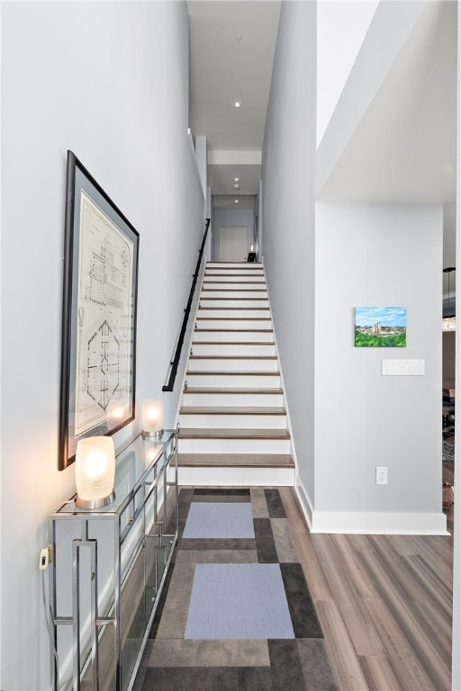 stairway with wood-type flooring and a towering ceiling