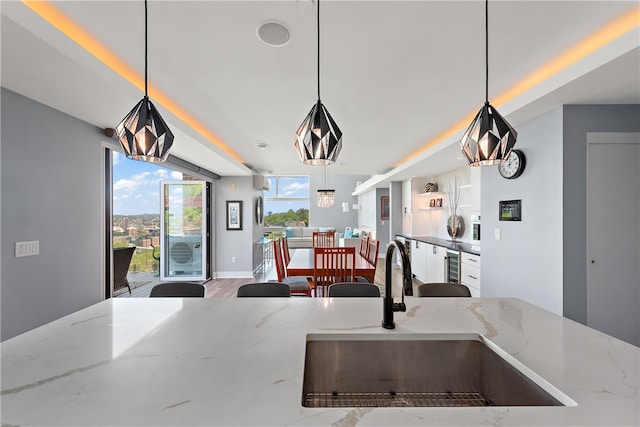 kitchen featuring sink, decorative light fixtures, wood-type flooring, and light stone countertops