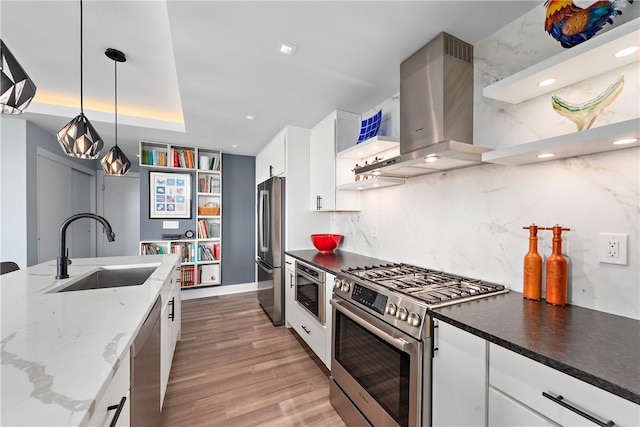 kitchen featuring light hardwood / wood-style flooring, wall chimney range hood, hanging light fixtures, appliances with stainless steel finishes, and sink