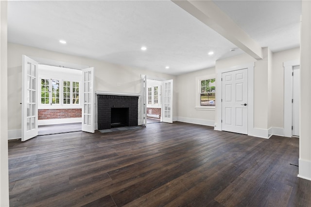 unfurnished living room featuring dark hardwood / wood-style floors, a brick fireplace, a wealth of natural light, and french doors