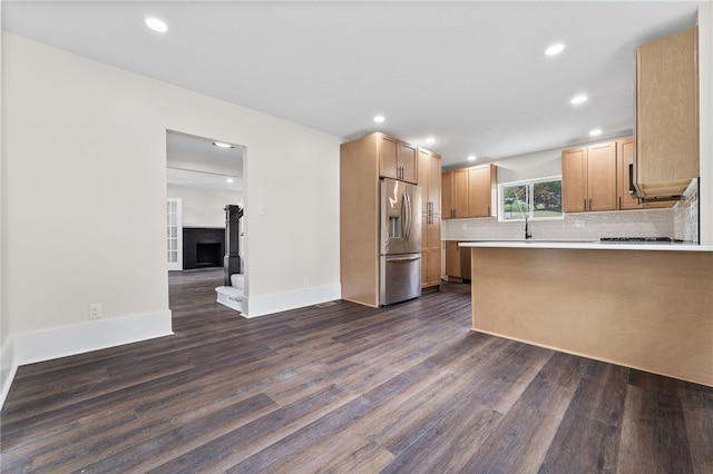 kitchen featuring tasteful backsplash, sink, a brick fireplace, stainless steel fridge with ice dispenser, and dark hardwood / wood-style flooring