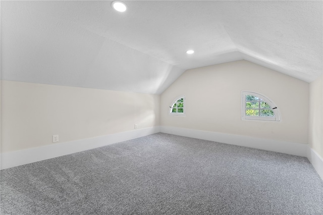 additional living space featuring carpet flooring, vaulted ceiling, and a textured ceiling