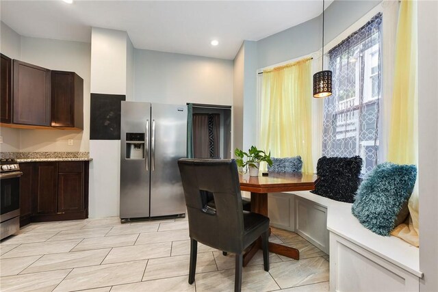 kitchen with light tile patterned floors, light stone counters, stainless steel appliances, pendant lighting, and dark brown cabinetry